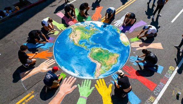 Volunteers painting giant chalk earth mural with colorful handprints on closed street