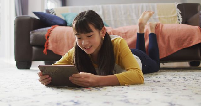 Asian girl smiling and using tablet lying on floor at home. childhood, technology and domestic life concept.