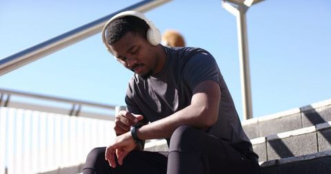 African american man checking smartwatch on outdoor steps while wearing headphones