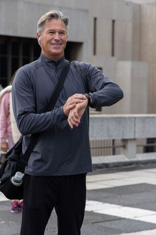 Middle-aged man checking smartwatch on urban bridge after outdoor workout