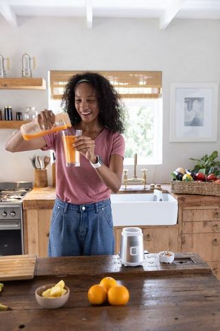 African american woman pouring fresh orange juice in rustic sunlit kitchen promoting health