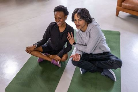 Diverse friends sitting on yoga mats chatting after workout with gymwear and smartwatches