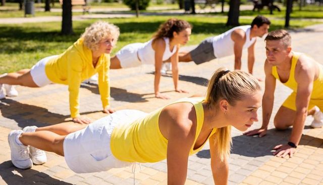 Outdoor group plank workout with blonde athlete leading park bootcamp in yellow apparel