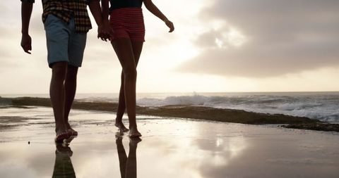Couple walking holding hands on beach pier at sunset