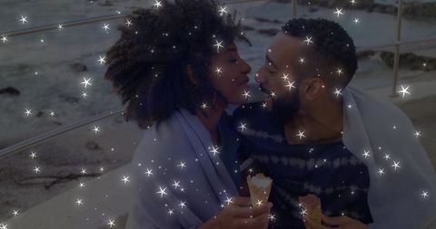 Romantic couple sharing ice cream by seaside at night