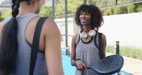 African american women chatting on padel court holding paddles and headphones