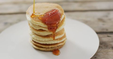Stack of pancakes with drizzling maple syrup on white plate