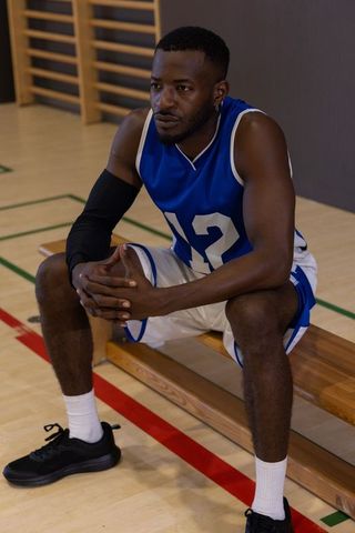 African american basketball player sitting on bench wearing blue #12 jersey focused