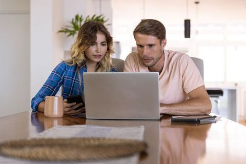 Couple Using Laptop Together at Home with Smartphones and Mug