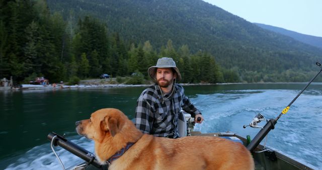 Man and dog enjoying a peaceful fishing trip on a mountain lake. The man is wearing a plaid shirt and a bucket hat, holding a fishing rod. The dog sits attentively on the front of the boat. Ideal for depicting outdoor adventures, relaxation in nature, and the bond between humans and animals.
