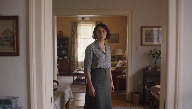 Woman standing in cozy vintage doorway wearing floral blouse and skirt, quiet portrait
