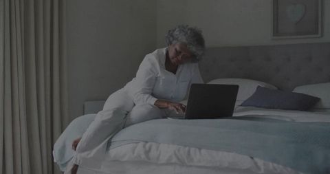 Senior Woman Relaxing in Bedroom on Laptop in Pajamas