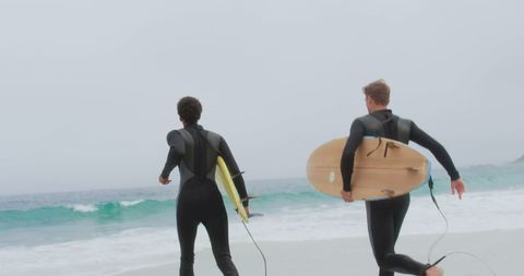 Two Male Surfers Running Towards Ocean on Sandy Beach