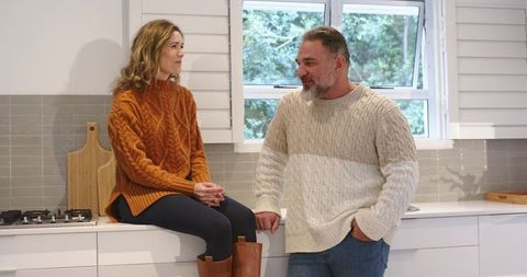 Couple Chatting on Sunlit Modern Kitchen Countertop Wearing Cozy Knit Sweaters