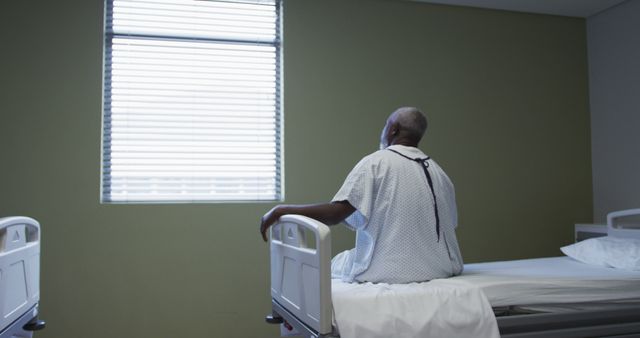 African american male patient sitting in hospital bed looking at window. medicine, health and healthcare services.