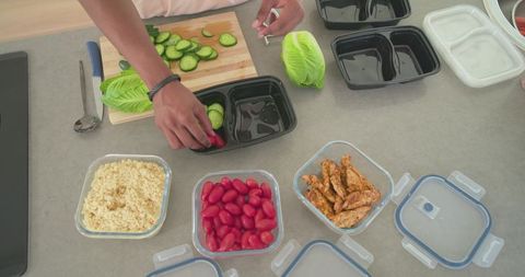 African american man packing meal-prep bowls with cherry tomatoes, quinoa, grilled chicken