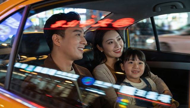 Smiling family riding yellow taxi at night with neon reflections and city lights
