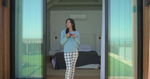 Serene morning balcony asian woman standing at glass doors holding mug overlooking ocean