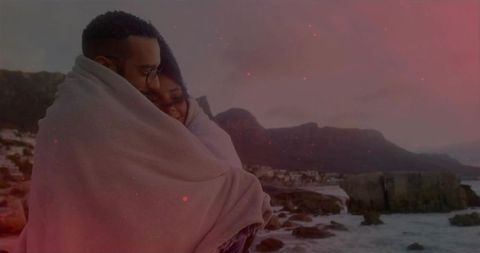 Couple Embracing on Rocky Shoreline at Twilight Wrapped in Blanket Sharing Warmth