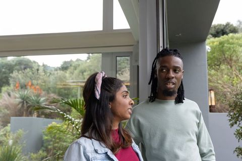 Diverse couple talking at modern glass doorway with lush courtyard plants and succulents