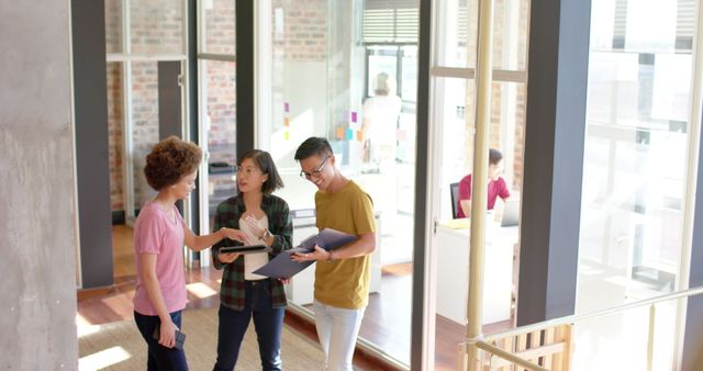 High angle of happy diverse male and female colleagues engaged in casual discussion in an office corridor. Ideal for representing team collaboration, modern work culture, startup atmosphere, or promotional material about inclusivity and communication in the workplace. Useful for business presentations, websites, and brochures focusing on team building, employee morale, and corporate diversity.