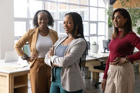 Diverse female team standing confidently in open-plan office demonstrating leadership
