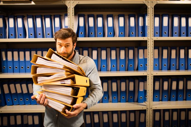Businessman holding stack of files against cabinet in storage room
