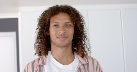 Confident Young Man with Curly Hair Smiling Indoors