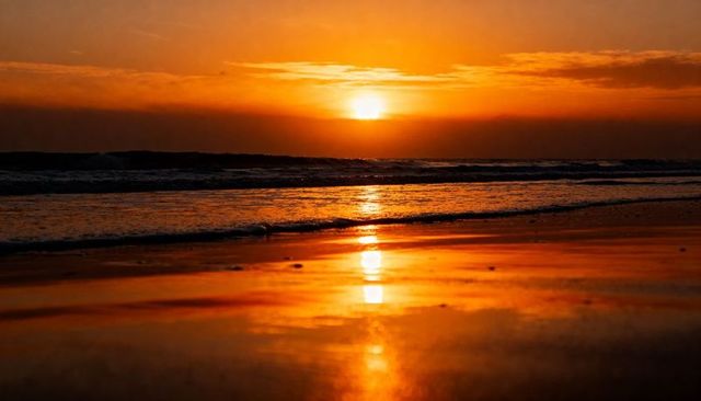 Sunset casting golden reflection on wet sand with vertical sun glare over ocean horizon