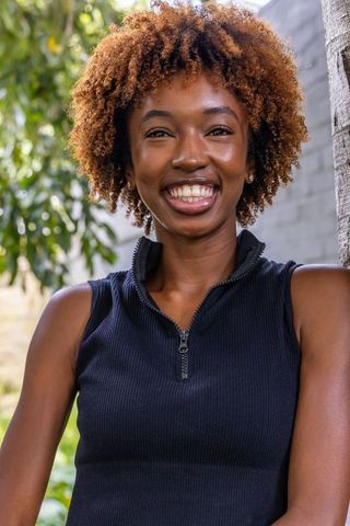 Joyful young woman smiling outdoors in sunlit garden wearing black ribbed zip-top