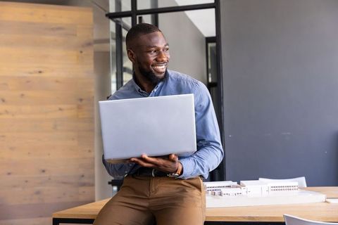 Architect Holding Laptop in Modern Office With Scale Model