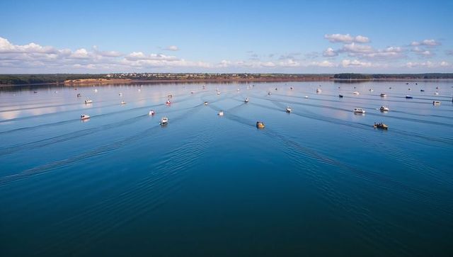 Boats gliding across calm estuary creating parallel wake patterns under blue sky