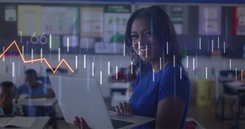Female teacher using laptop with overlay of financial data in classroom