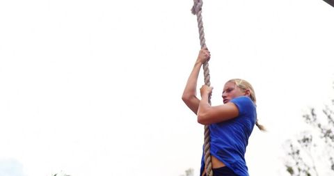 Athletic woman climbing thick rope at outdoor fitness course showing strength and focus