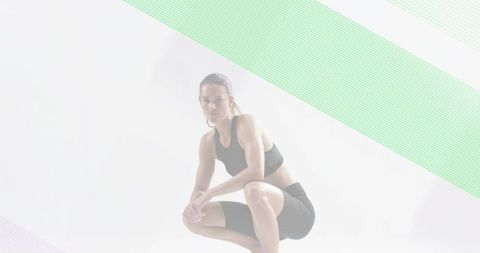 Female athlete squatting in minimal high-key background wearing black activewear and hoops