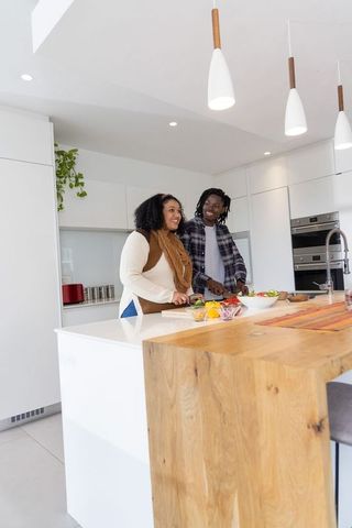 African american couple preparing salad at modern minimalist kitchen island with wood counter