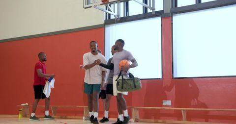 Post-game greeting between diverse teammates on basketball court holding ball and duffel bag