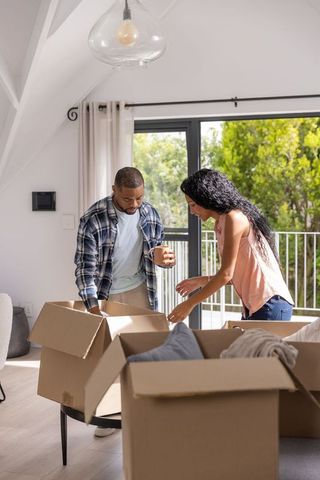Couple unpacking boxes in bright modern living room with balcony