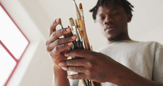 African american male painter choosing brushes in artist studio. art, creative and leisure time concept.