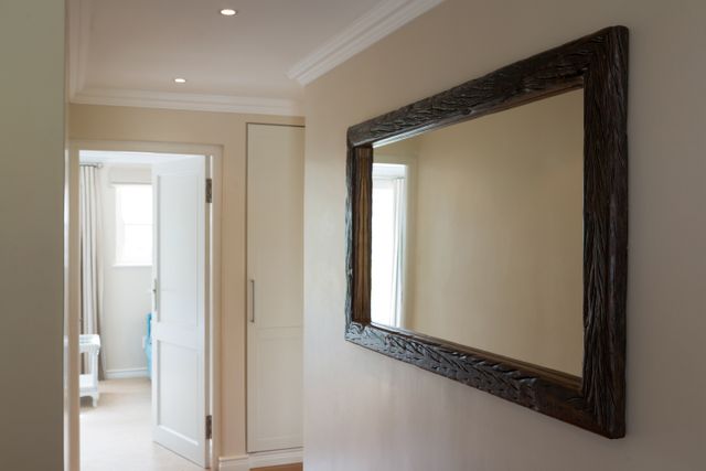Wooden framed mirror hanging on a white wall in a modern home hallway. The minimalist design and clean lines create an elegant and stylish look. Ideal for use in articles or advertisements related to interior design, home decor, and modern living spaces.