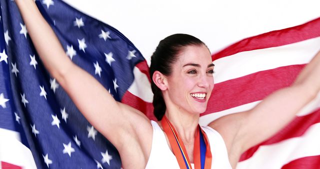 Woman celebrating a victorious moment lifting an American flag whilst wearing medals around her neck. Ideal for themes related to sports victories, patriotism, national pride, athletic achievements, and American sports events.