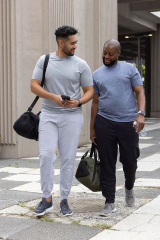 Friends walking and chatting in gymwear carrying duffel bags and water bottle