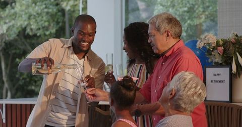Multigenerational family celebrating retirement on patio pouring champagne into flutes