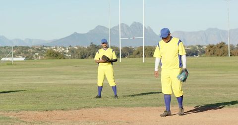 Baseball teammates walking on infield holding gloves in yellow uniforms with mountain background