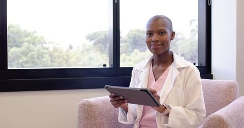 African female doctor holding tablet while sitting on pink chair in bright clinic