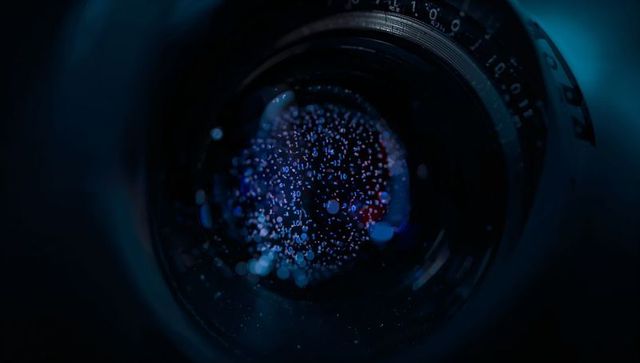 Macro camera lens reflecting digital bokeh and binary code in moody cyan-blue optical glow