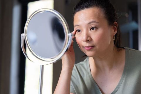 Mature asian woman inspecting skin with magnifying mirror at home vanity morning routine