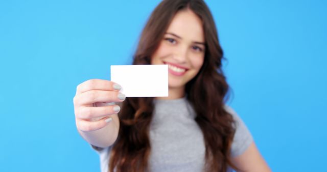A young Caucasian woman smiles as she presents a blank card to the camera, with copy space. Her cheerful expression and the card's prominence suggest an invitation or an opportunity for branding and personalization.