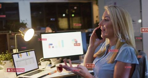 Businesswoman talking on phone while working late at desk with laptop charts and graphs
