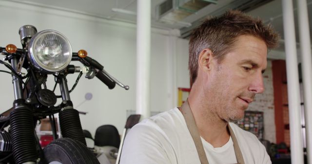 Man working in motorcycle repair shop with vintage bike in background - Download Free Stock Images Pikwizard.com